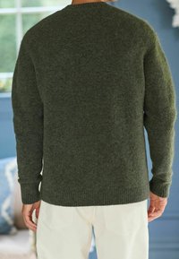 Dark green wool sweater with long sleeves, ribbed cuffs and hem, featuring a simple round neckline and a soft, textured finish.