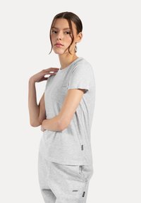 Camiseta de cuello redondo en gris claro, fabricada con una tela suave y de manga corta, que presenta un pequeño logo en el pecho y un corte relajado.