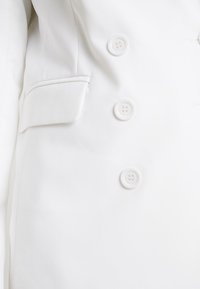 Biała marynarka z podwójnym zapięciem, gładkim materiałem, sześcioma guzikami i boczną kieszenią z klapą.