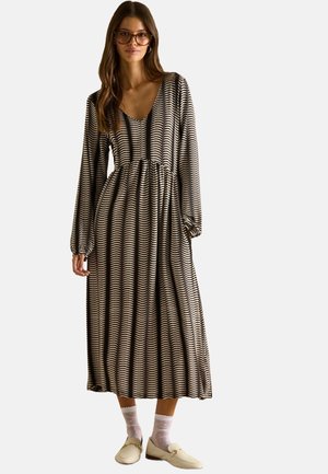 Long-sleeve, V-neck dress in black and cream wave pattern. Soft fabric with a gathered waist. Paired with cream slip-on shoes and white socks.