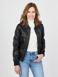 Schwarze Lederjacke mit taillierter Passform und gerippten Bündchen. Getragen über einem weißen Rollkragenpullover, kombiniert mit hochgeschnittenen blauen Jeans.