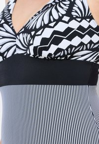 Maillot de bain deux pièces noir et blanc avec des motifs floraux et géométriques, une bande noire unie à la taille, et une section inférieure rayée.