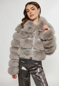 Šedá krátká bunda z faux kožešiny s horizontálními pruhy, má vysoký límec a zapínání na zip. Doplněná lesklými metalickými kalhotami.