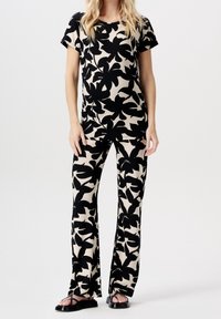 Černý a béžový květinový vzorovaný top a odpovídající rozšířené kalhoty, vyrobené z měkké látky, s krátkými rukávy a volným střihem. Černé sandály.
