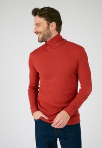 Red turtleneck long-sleeve shirt with a smooth texture, fitted design, and ribbed cuffs, paired with dark blue denim jeans.