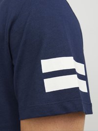 Marineblå t-shirt med en glat bomuldsstruktur og hvide striber på ærmet. Enkelt, moderne design der er velegnet til afslappet brug.