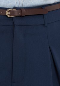 Gros plan sur un pantalon bleu marine avec une ceinture en cuir marron et une boucle dorée, associé à un haut en maille bleu clair.
