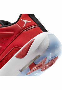 Rode sneaker met een bovenwerk van mesh en leer, witte tussenzool, transparante buitenzool en een zilveren logo aan de zijkant. Opvallende textuuraccenten zichtbaar.