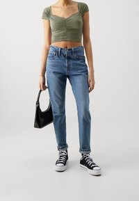 Top corto verde oliva con dettaglio arricciato, jeans a vita alta blu chiaro, borsa a mano in patent nero e sneaker alte nere.