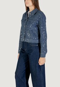 Giacca di jeans cropped di colore blu scuro con paillettes argentate. Presenta chiusura anteriore con bottoni, colletto a punta e due taschini sul petto.