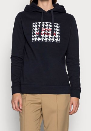 Felpa navy con cappuccio e cordino, caratterizzata da un motivo houndstooth e logo "TOMMY HILFIGER" in rosso. Realizzata in tessuto morbido e testurizzato.