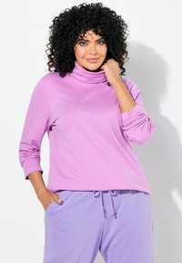 Maglione a collo alto viola con maniche lunghe, dalla consistenza morbida. Abbinato a pantaloni jogger lavanda, dotati di coulisse e tasche laterali.