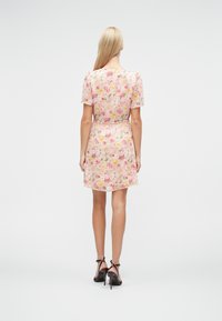 Φλοράλ φόρεμα α πό απαλό, διάφανο ύφασμα· διαθέτει κοντά μανίκια, εφαρμοστό μπούστο και φούστα με βολάν με ρόζ, κίτρινες και πράσινες λεπτομέρειες.