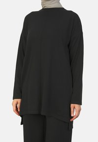Zwarte longsleeve top met een ronde hals, een losse pasvorm en zijsplitten voor extra comfort. Gemaakt van een zachte stof met een gladde textuur.