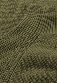 Gros plan sur un tissu vert tricoté montrant des motifs de côtes variés et un fil texturé.