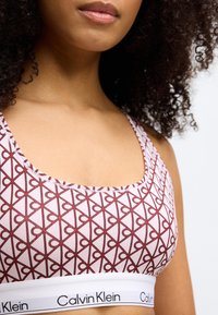 Calvin Klein bralette in light pink with a maroon heart pattern. Features a wide white band with the brand name printed. Soft, stretchy fabric.