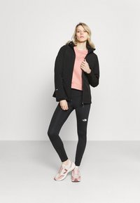 Zwarte waterdichte jas, roze sweatshirt, zwarte leggings met logo en roze sneakers. Glad textuur en atletische pasvorm.