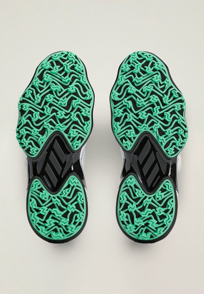 Suela de zapatos en negro con un patrón texturizado que presenta acentos de goma verde. El diseño incluye líneas onduladas y formas geométricas para el agarre.