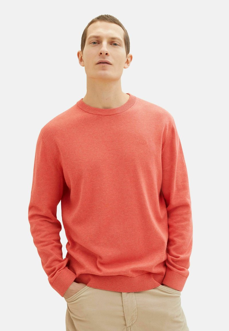 Koralsweater lavet af strikket stof med rund hals og lange ærmer. Den har ribbede manchetter og kant, samt en diskret logo detalje.