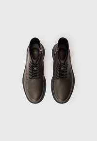 Pantofi din piele neagră cu un superior texturat, sistem de închidere cu șireturi și fermoar pe lateral. Prezintă un vârf rotund și o talpă din cauciuc contrastantă.