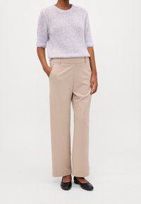 Ljuslila stickad tröja med korta ärmar, beige höga vida byxor och svarta platta skor. Enkel, strukturerad design.