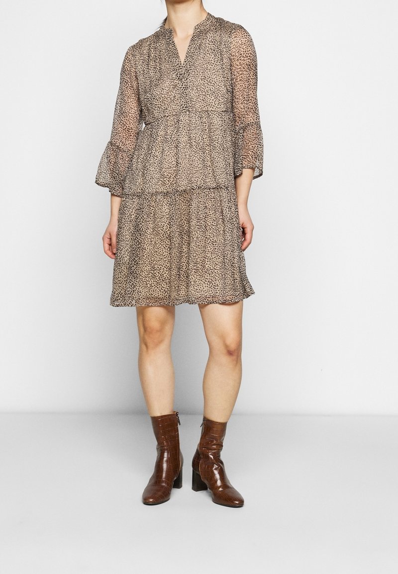 Ruskea eläinkuosilla varustettu mekko, jossa on V-kaula-aukko, kolmanneksen mittaiset hihat ja kerroksittainen muotoilu; yhdistetty ruskeisiin teksturoiduille nilkkabootseille.