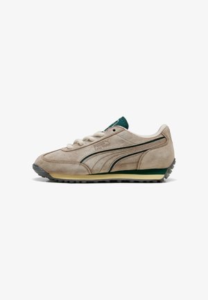 Beige suede sneakers met groene accenten, vetersluiting en opvallende PUMA-branding. Beschikt over een geprofileerde zool voor grip en stabiliteit.