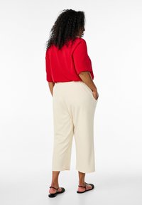 Rood kort mouwtopje gecombineerd met crèmekleurige, driekwart broek met zijzakken, een gladde textuur en zwarte sandalen.