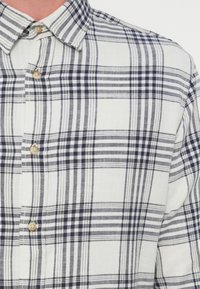 Ανδρικό πουκάμισο καρό σε λευκό και ναυτικό μπλε, με γιακά που κουμπώνει με κουμπιά, μαλακό υφασμένο ύφασμα και καρό μοτίβο με στρογγυλά κουμπιά.