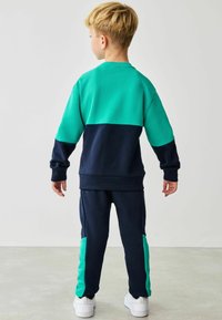 Drengevare i teal og navy blå. Toppen har et farveblokdesign, mens bukserne har teal detaljer i siderne. Fremstillet af blødt stof.