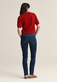 R�ød kortærmet striktrøje parret med mørkeblå slim-fit jeans og lysebrune sneakers. Blød tekstur, minimalistisk design og klassisk pasform.