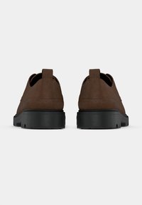 Par smeđih casual cipela od brušene kože s debelim crnim gumenim potplatima, prikazane s leđa na jednobojnoj bijeloj pozadini.