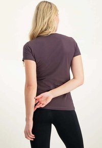 Lyhythihainen, istuva viininpunainen t-paita, jossa on sileä pinta, pyöreä kaula-aukko ja minimaaliset saumuriyksityiskohdat, yhdistetty mustiin legginsseihin.