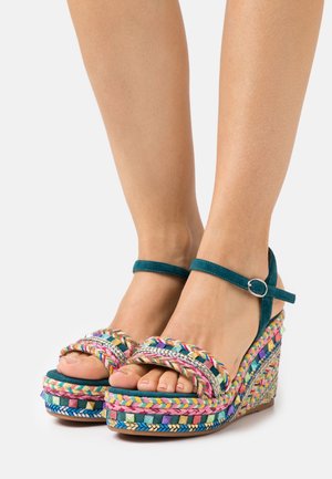 Sandały na koturnie z kolorowym, plecionym paskiem, turkusowym paskiem wokół kostki i wielokolorową, plecioną platformą. Teksturowane i lekkie materiały.