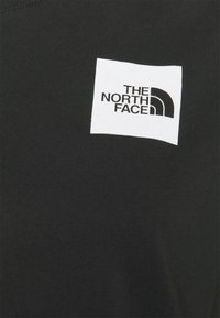 T-shirt in cotone nero con logo quadrato bianco recante la scritta "THE NORTH FACE" e un design a mezza arcata. Tessuto liscio, maniche corte.
