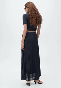 Ensemble deux pièces en tricot côtelé sombre comprenant un haut court à manches courtes et une longue jupe plissée. Le tissu a une texture douce.