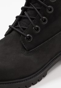 Stivale da trekking in suede nero con lacci rotondi, occhielli in metallo e suola in gomma testurizzata. Include dettagli cuciti lungo il lato.
