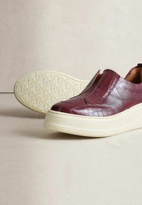 Burgunderfarvede slip-on sko lavet af tekstureret læder, med en tyk cremefarvet sål og en glat indre foring.