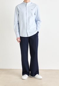 Ljusblå långärmad skjorta med knappar och rund krage, ihop med mörkblå vida byxor och vita sneakers. Enkelt mönster, inga motiv.