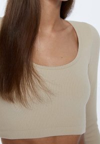 Beige geripptes Crop-Top mit weitem, rundem Halsausschnitt und langen Ärmeln, das eine enge Passform und eine glatte Textur aufweist.