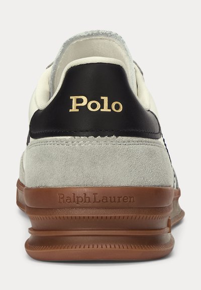 Vedere din spate a unei adidași gri și negri cu talpă maro, cu inscripția „Polo” aurie pe eticheta călcâiului și „Ralph Lauren” embossat pe talpă.