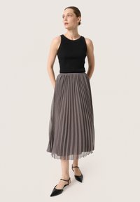 Een zwarte geribbelde tanktop gecombineerd met een grijze plissé midi-rok. De outfit heeft een gladde textuur en subtiele beweging. Zwarte puntige ballerina's maken de look compleet.