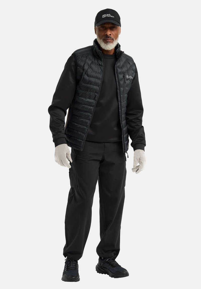 Black puffer vest with a zip front, black sweatshirt, and cargo pants. Black gloves and shoes complete the outfit. Cap features logo.
