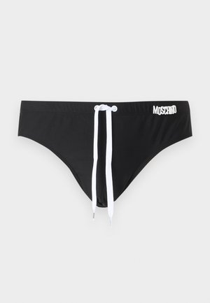 Mustad madala vöökohaga ujumispüksid valge nööriga ja valge Moschino logoga vöö paremal küljel, heleda ühevärvilise taustaga.