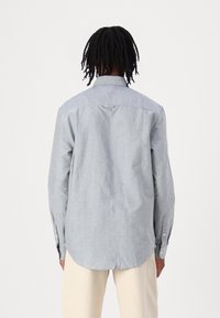 Ljust blå långärmad skjorta med mjuk textur, knäppta ärmslut och en rundad nederkant. Har en klassisk krage och en ögla på baksidan.