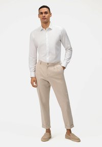 Witte langemouwen overhemd met knopen, gecombineerd met lichtbeige geplooide broeken en beige instappers. Soepele stof, tailored fit en opgerolde mouwen.