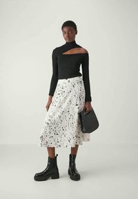 Black long-sleeve top with cutout, white midi skirt with black splatter pattern, and black chunky boots. Holding a black handbag.