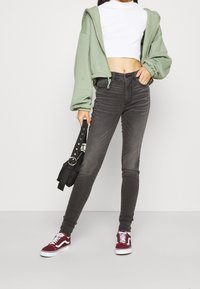 Jeans gris ajustados, un top blanco corto y un sudadera con capucha verde claro. Los accesorios incluyen un bolso negro pequeño y zapatillas burdeos.