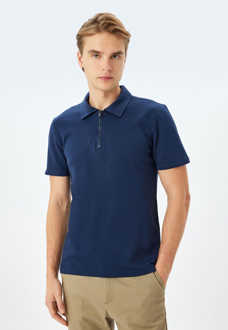 Marineblauwe polo met een kraag, korte mouwen en een kwart rits aan de voorkant. Gemaakt van gladde katoenstof, met een getailleerd ontwerp.