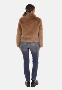 Giacca in pelliccia sintetica marrone con colletto alto, texture morbida e maniche lunghe, abbinata a jeans blu e scarpe nere chunky, vista da dietro.